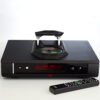 Otvoreni top-loading mehanizam Rega Isis CD playera s umetnutim diskom i priloženim metalnim daljinskim upravljačem